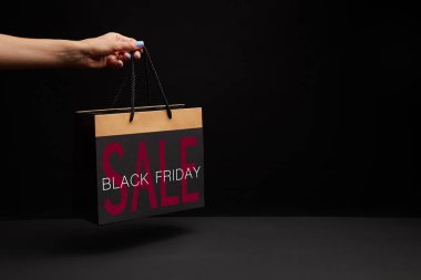 partial view of woman holding black shopping bag with black friday sale clipart