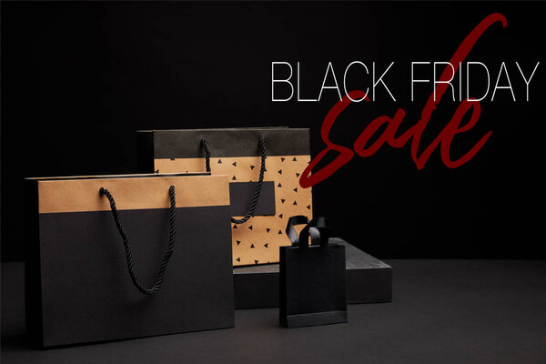 close up view of shopping bags arranged on black background with black friday sale
