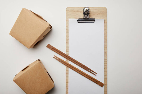 top view of blank menu, wok boxes and chopsticks on white surface 