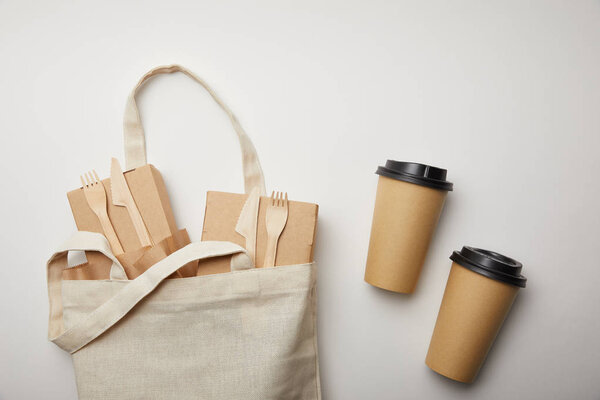 elevated view of cotton bag with food boxes and two disposable coffee cups on white surface