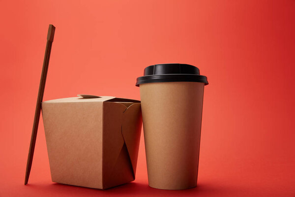 close up view of noodle box, paper cup of coffee with chopsticks on red, minimalistic concept