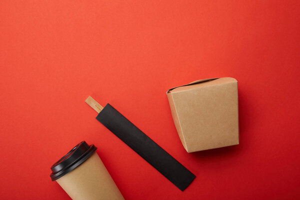 top view of noodle box, paper cup of coffee with chopsticks on red, minimalistic concept