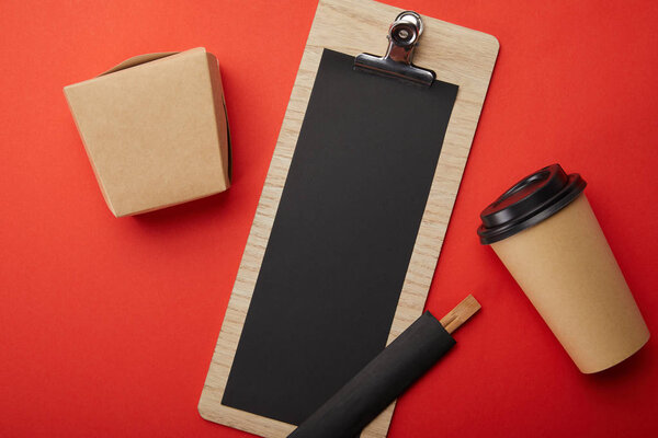 flat lay with arranged disposable coffee cup, chopsticks, wok box and blank menu on red surface