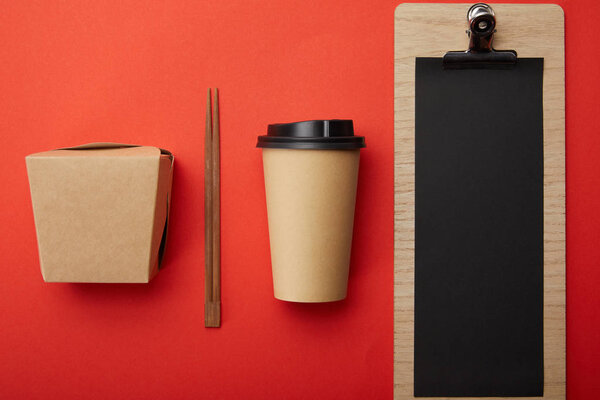 top view of arranged disposable coffee cup, chopsticks, wok box and blank menu on red surface