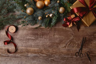 ahşap masa üzerinde Noel hediye kutuları, köknar çelenk, şerit biriktirme ve makas üstten görünüm