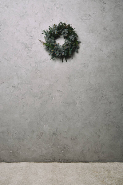 зеленый еловый венок для украшения Рождества висит на серой стене в комнате
