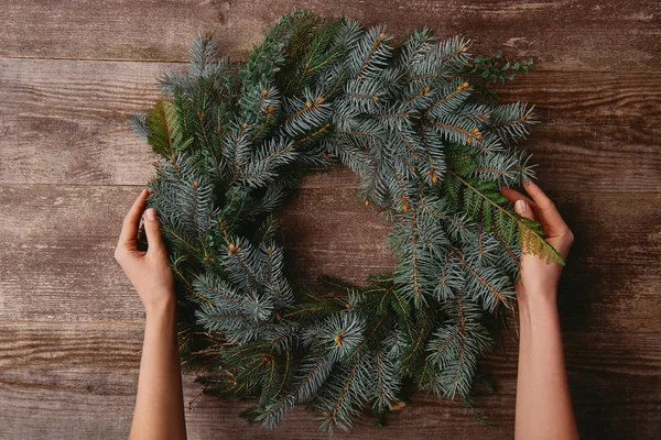 Imagen Recortada Mujer Sosteniendo Corona Abeto Navidad Mesa Madera — Foto de Stock