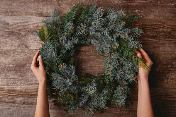 cropped image of woman holding christmas fir wreath at wooden table