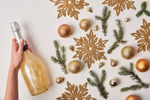 cropped image of woman holding bottle of sparkling champagne near christmas decoration isolated on white