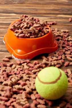 ahşap masa üzerinde köpek maması ve topu ile plastik kase görünümünü kapat