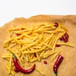 Top view of french fries with spicy peppers on parchment paper isolated on white