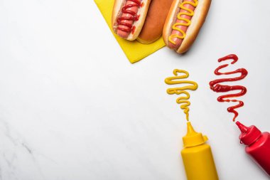 top view of delicious hot dogs with mustard and ketchup on white marble surface clipart