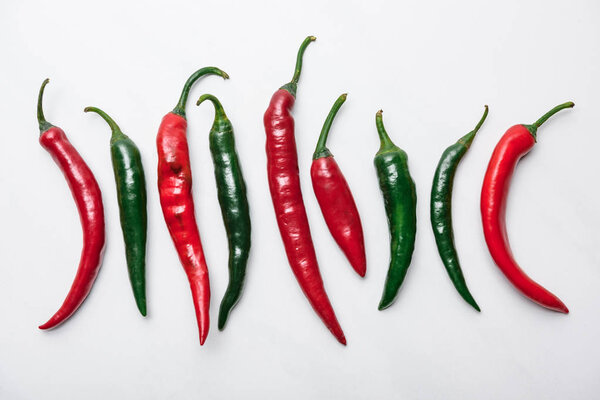 top view of red and green chili peppers in row on white marble tabletop
