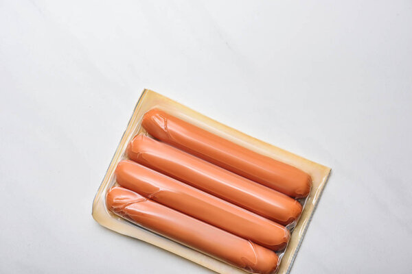 top view of plastic package of sausages on white marble surface