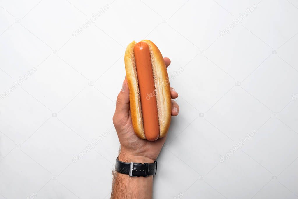 cropped shot of man holding tasty hot dog on white marble surface
