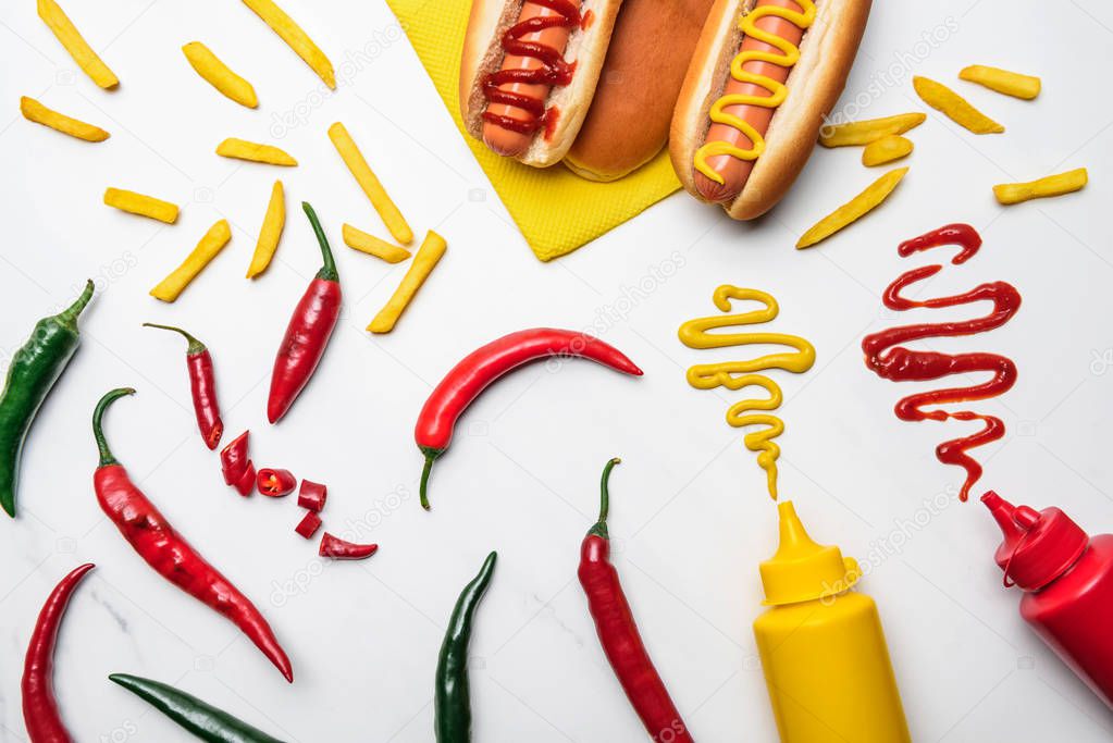 top view of delicious hot dogs and peppers with mustard and ketchup on white marble surface