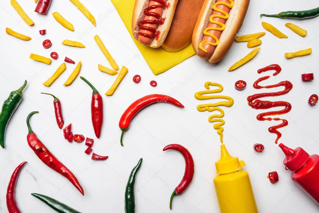 top view of delicious hot dogs, peppers and fries with mustard and ketchup on white surface