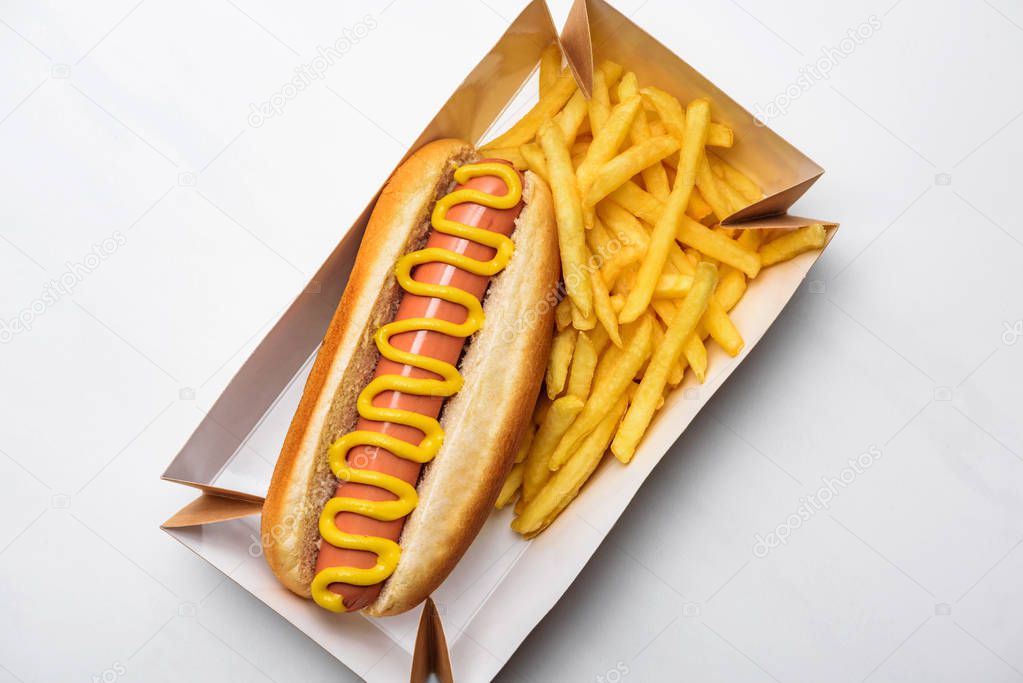 top view of tasty hot dog with fries in cardboard tray on white