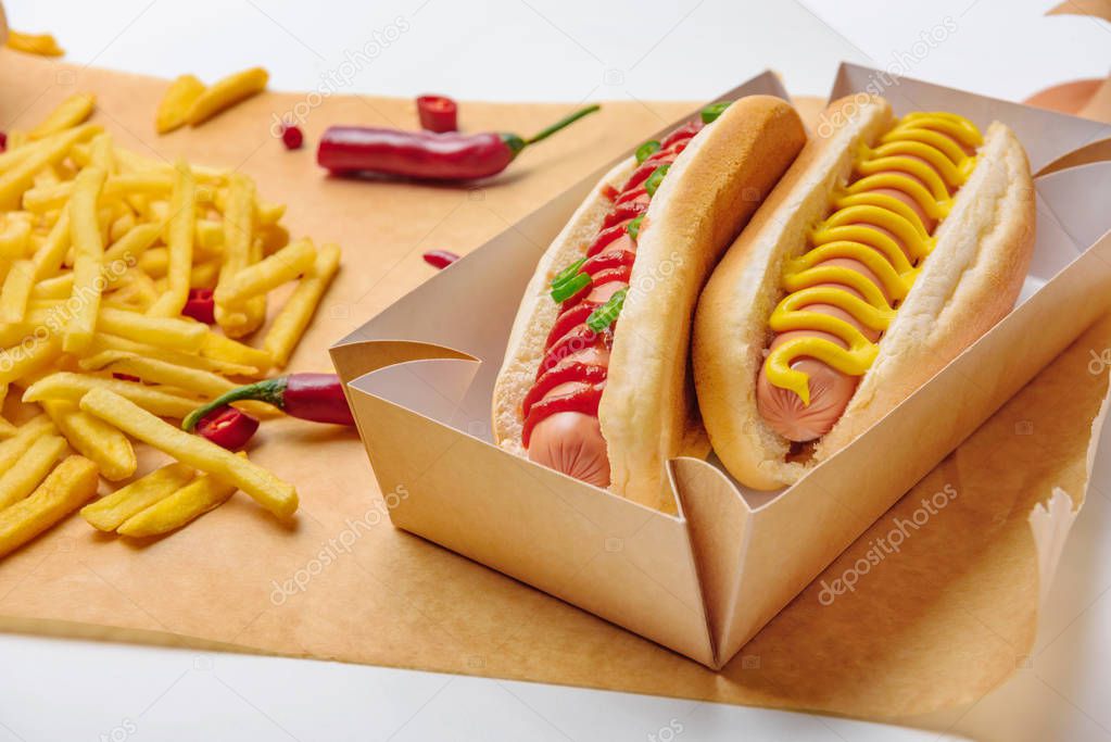 close-up shot of spicy hot dogs with french fries on parchment paper