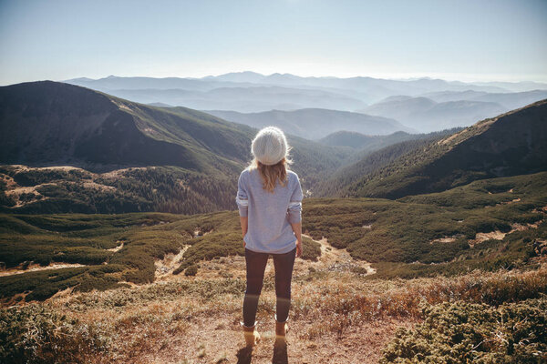 back view of female traveler looking at beautiful mountains on sunny day, Carpathians, Ukraine