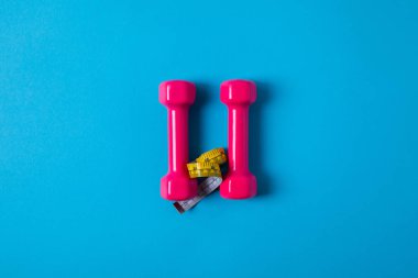 Ölçüm bandı ve pembe dumbbells izole mavi, minimalist kavramı üzerinde sarı yukarıdan görüntülemek 