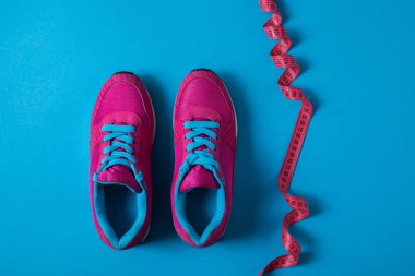 view from above of pink sport shoes and measuring tape isolated on blue, minimalistic concept  clipart