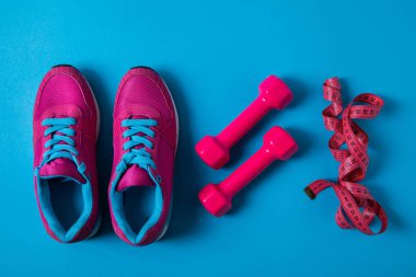 Düzenlenmiş pembe spor ayakkabıları ile halter yat ve teyp ölçme izole mavi, minimalist kavramı üzerinde satır yerleştirilir 