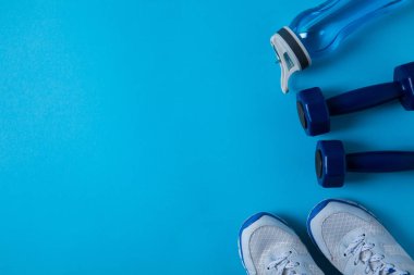 elevated view of dumbbells, sneakers and sport bottle with water isolated on blue 