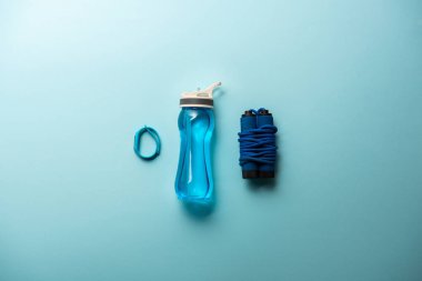 flat lay with fitness tracker, sport bottle and jump rope placed in row isolated on blue, minimalistic concept  clipart