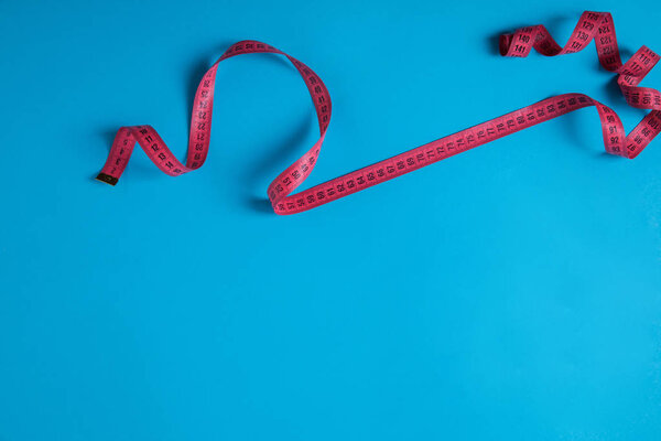 top view of pink measuring tape isolated on blue, minimalistic concept 