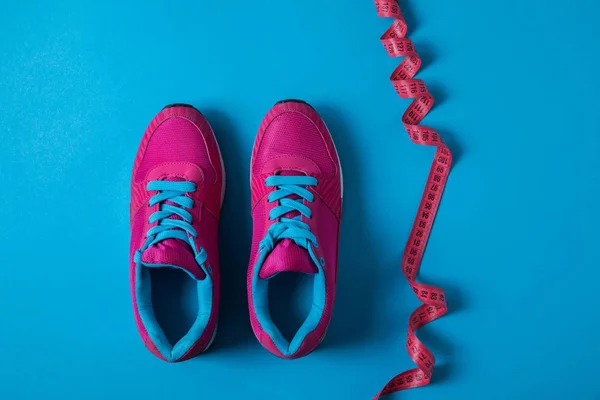 从上面的粉红色运动鞋和测量磁带隔离在蓝色 简约的概念 — 图库照片