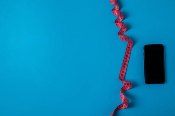 top view of pink measuring tape and smartphone with blank screen isolated on blue, minimalistic concept 