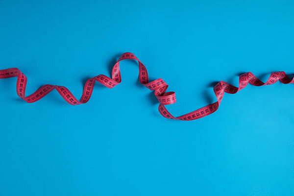 top view of pink measuring tape isolated on blue, minimalistic concept 