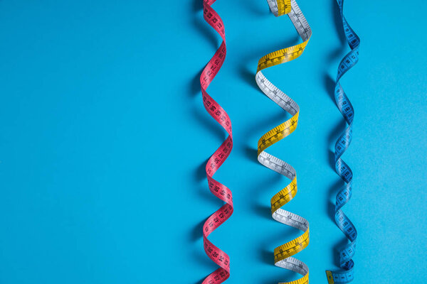 flat lay with arranged colorful measuring tapes placed in row isolated on blue