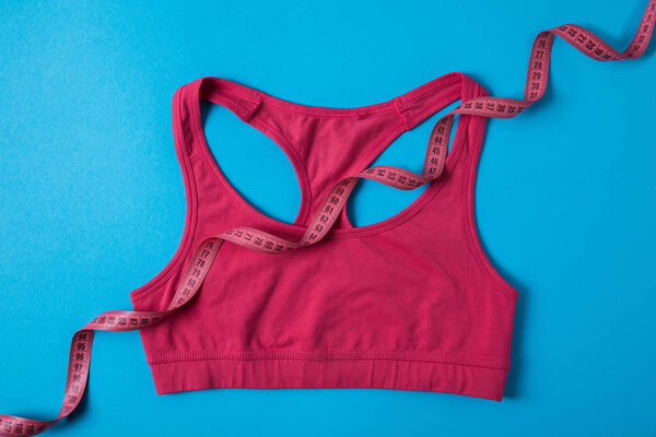 elevated view of pink sports bra and measuring tape isolated on blue, minimalistic concept 