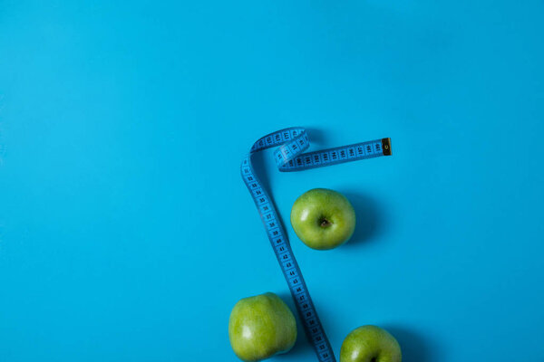 top view of delicious green apples and measuring tape isolated on blue 