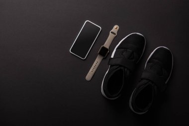 Düzenlenmiş smartphone, smartwatch ve izole siyah, minimalist kavramı üzerinde spor ayakkabı üstten görünüm 