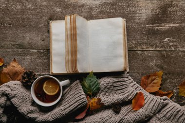 düz lay gri kazak ve fincan çay, boş defter ve ahşap masa üstü düşmüş yaprakları ile