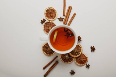 flat lay with arranged cinnamon sticks, anise stars, dried orange pieces and cup of hot tea on white background clipart
