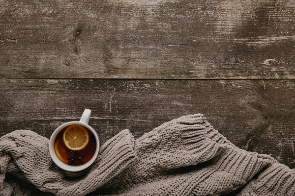 flat lay with grey sweater and cup of tea with lemon pieces on wooden tabletop