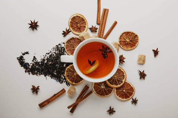 flat lay with arranged cinnamon sticks, anise stars, brown sugar and cup of hot tea on white background
