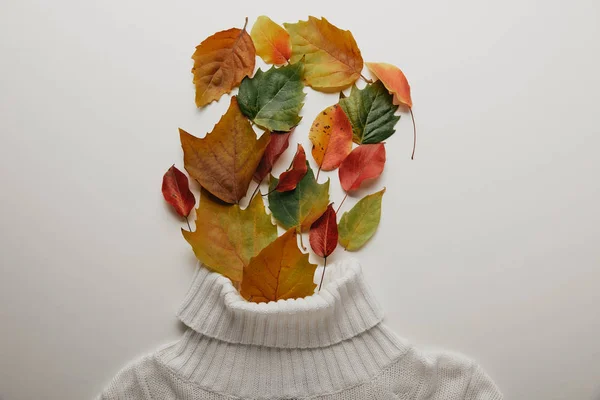 top view of white woolen sweater and fallen leaves arranged on white surface
