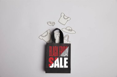 top view of paper bag with black friday sale inscription and paper clothes on grey background clipart