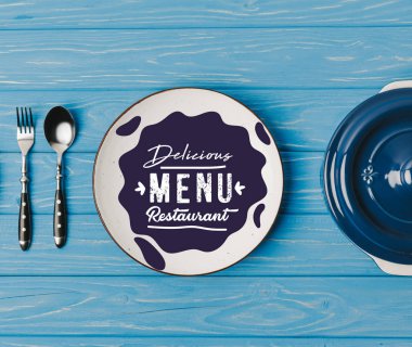 top view of fork, spoon and plates on blue table, delicious menu restaurant lettering clipart