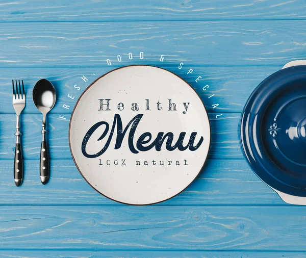 Top view of fork, spoon and plates on blue table, healthy menu lettering — Stock Image Top View Fork Spoon Plates Blue Table Healthy Menu Lettering Stock Picture