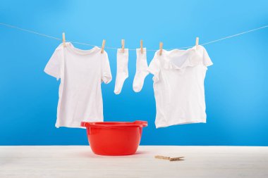 red basin, clothespins and clean white clothes hanging on rope on blue  clipart