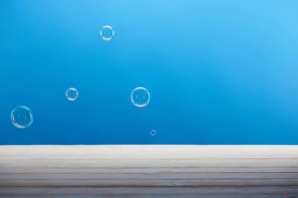 clean soap bubbles and white wooden surface on blue background