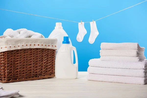 laundry basket, plastic containers with laundry liquids, pile of clean soft towels and white socks hanging on rope on blue