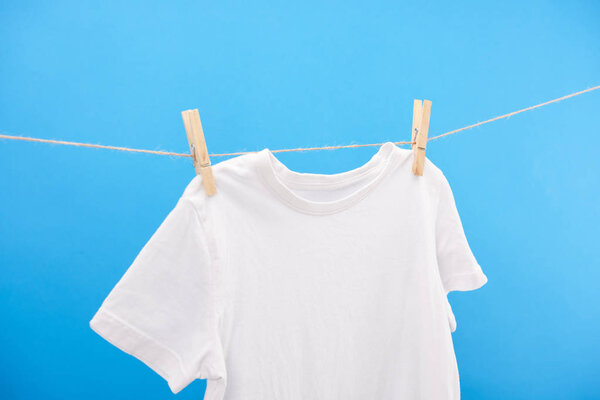 close-up view of clean white t-shirt hanging on clothesline isolated on blue    