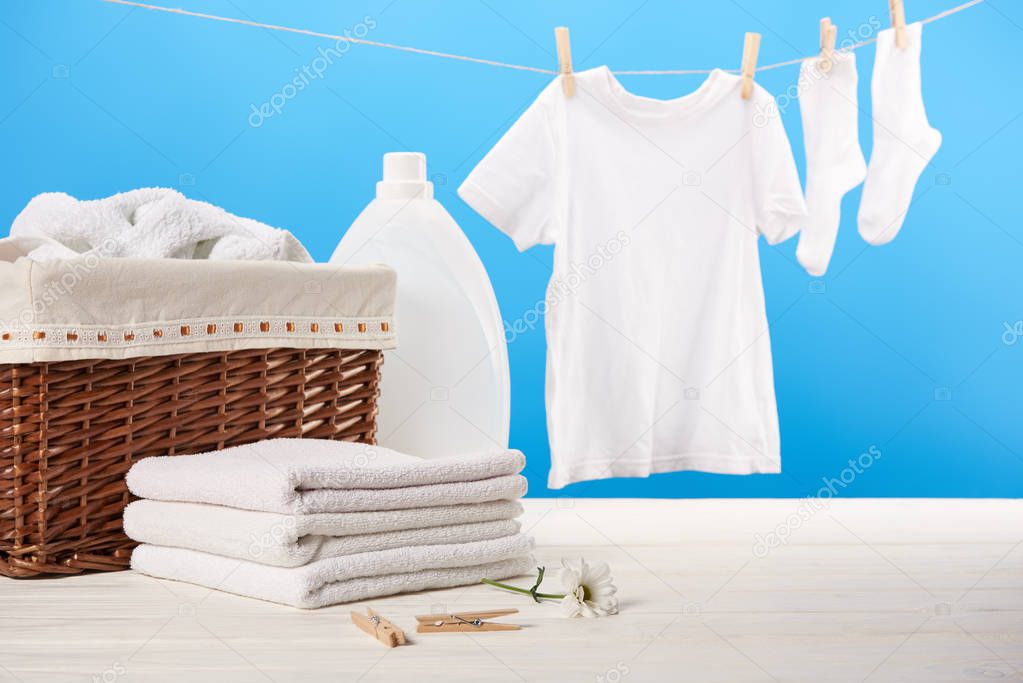 laundry basket, plastic container with laundry liquid, pile of clean soft towels and white clothes hanging on clothesline on blue  